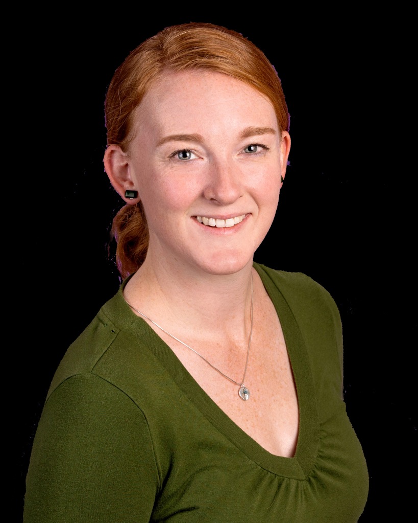 a white woman with red hair and blue eyes wearing a green v-neck shirt smiles at the camera